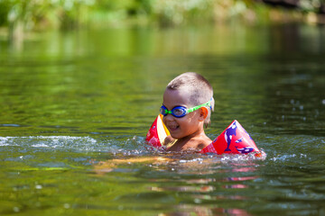 Cute boy is swimming in the small river with his armbands and goggles