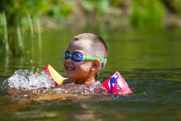Cute boy is swimming in the small river with his armbands and goggles