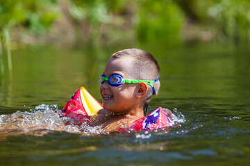 Cute boy is swimming in the small river with his armbands and goggles