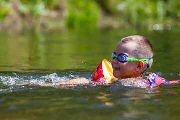 Cute boy is swimming in the small river with his armbands and goggles