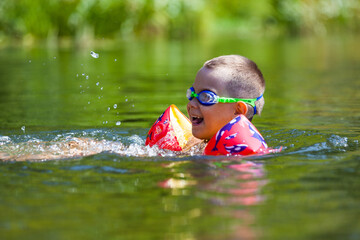 Cute boy is swimming in the small river with his armbands and goggles