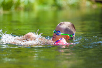 Cute boy is swimming in the small river with his armbands and goggles