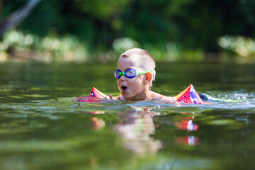 Cute boy is swimming in the small river with his armbands and goggles