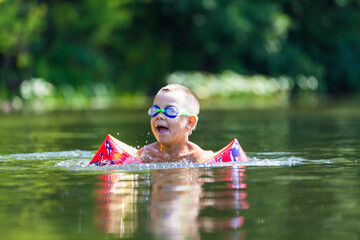 Cute boy is swimming in the small river with his armbands and goggles