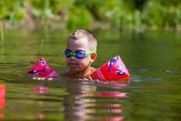 Cute boy is swimming in the small river with his armbands and goggles