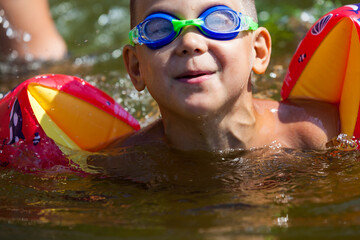 Cute boy is swimming in the small river with his armbands and goggles