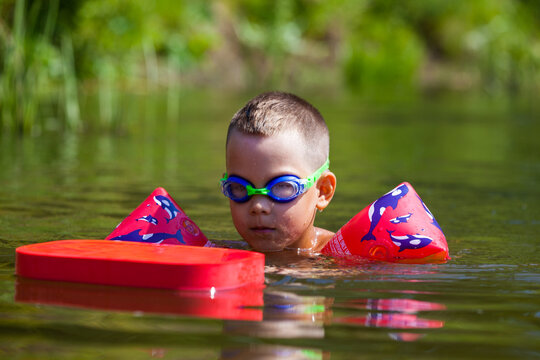 Cute boy is swimming in the small river with his armbands and goggles