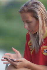young woman in red t-shirt with wet hair sit on the chair on the rock beach, looking afford on the sea. mountain on the background