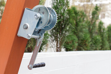 Mechanism of a metal winch on a painted wooden beam. Device of the veranda of the summer cafe. Copy space.