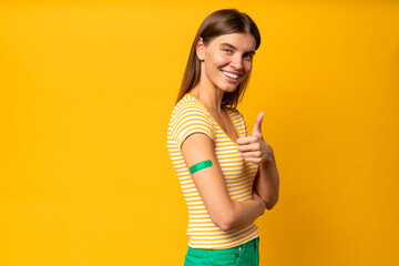 Young woman showing thumb up and another arm with band aid after coronavirus vaccine injection - obrazy, fototapety, plakaty