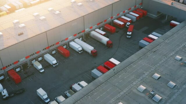 Logistics park with warehouse and semi-trailers trucks standing at warehouse ramps for loading and unloading goods. Aerial view