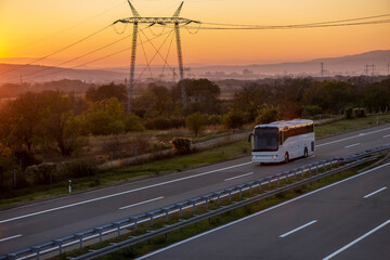 Fototapeta na wymiar White Modern comfortable tourist bus driving through highway at bright sunny sunset. Travel and coach tourism concept. Trip and journey by vehicle