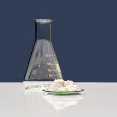 Obraz premium Closeup chemical ingredient on white laboratory table. Calcium carbonate Chip in Chemical Watch Glass place next to Erlenmeyer flask. Side View