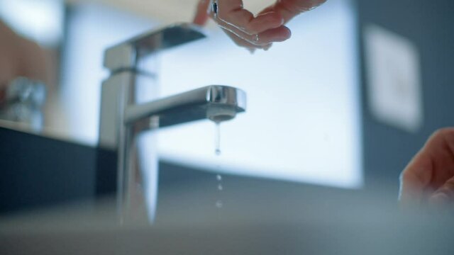 Caucasian man rinses his hands in slow motion and closes the tap in a modern bathroom.