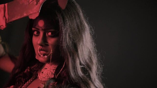 Angry Indian Goddess Kali looks at camera and brings out tongue, Indian goddess cosplay with long hair and dark background, slow motion
