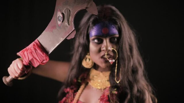 Live Indian Goddess Kali looks at camera with sword, Indian goddess cosplay with long hair and dark background