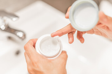 Woman's hands holding a pot of moisturizing cream.