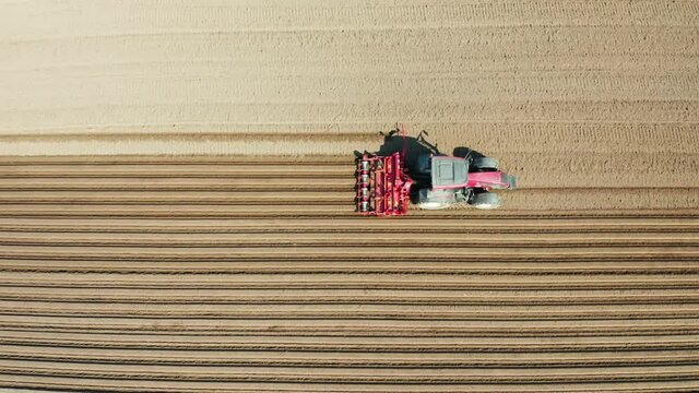 aerial view tractor cuts furrows in farm field for sowing farm tractor with rotary harrow plow preparing land for sowing. Tractor with harrows prepares the agricultural land for planting crop