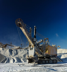 Obraz premium Heavy quarry excavator against the background of dark blue sky in a winter sunny day, panorama.