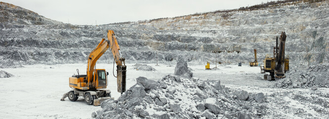 Panorama of a limestone quarry with heavy mining machinery - hydraulic hammer, excavator and...
