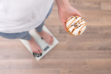 A woman stands on the scales, holds a donut in her hands, top view, copy space.