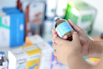 Pharmacist hand holding potion bottle reading the label medical information in drugstore.