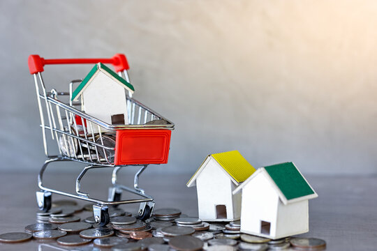 Miniature house and shopping cart medels with coin spilling on table. Real estate development or property investment. Construction industry business concept.
