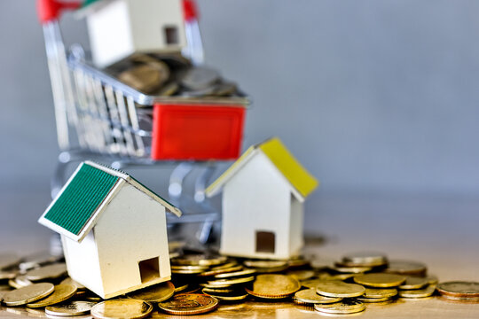 Miniature house and shopping cart medels with coin spilling on table. Real estate development or property investment. Construction industry business concept.