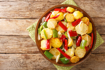 Patatas a lo pobre is a simple potato dish from Andalusian cuisine made of sliced potatoes are fried in olive oil with onion and peppers close up in the plate on the table. Horizontal top view