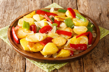 Rustic recipe for fried potatoes with onions and red and green peppers close-up in a plate on the table. horizontal