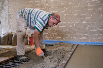 Construction worker spreading concrete above the radiant underfloor system.
