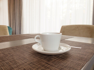 A white cup of tea with a saucer is on the table, behind is a window. Copspace