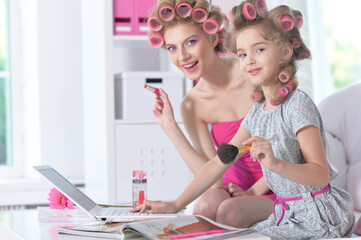 Mother and little daughter with hair curlers applying  make up