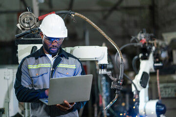 Male automation engineer checking and inspection control a robot arm welding machine with laptop...