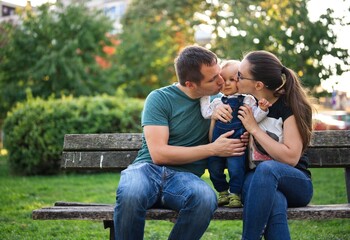 Couple sitting on a bench in a park holding their little child