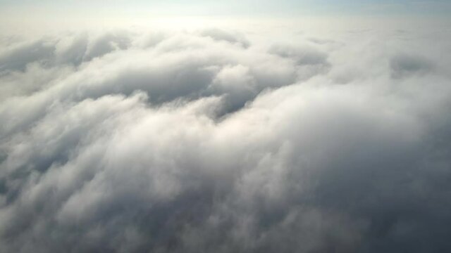 Aerial shot of flying over a layer of soft clouds at dawn