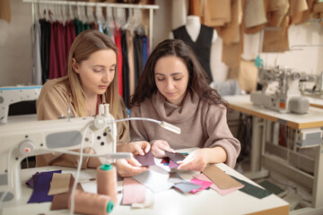 Two young dressmaker or designer colleagues working and discussing fashion project designers and look through fabric samples for clothes, profession and job occupation