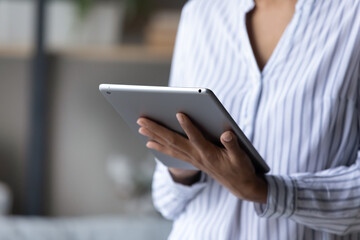 Cropped close up of African American woman holding tablet in hands, typing on screen, writing message in social network, young female chatting or shopping online, browsing electronic device apps