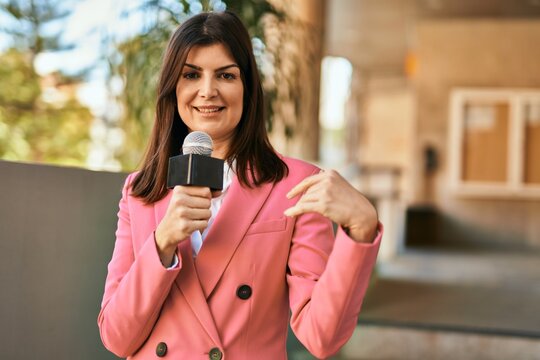 Middle age reporter woman holding microphone doing television speech outdoors