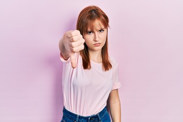 Obraz na płótnie Canvas Redhead young woman wearing casual pink t shirt looking unhappy and angry showing rejection and negative with thumbs down gesture. bad expression.