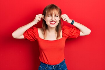 Redhead young woman wearing casual red t shirt smiling pulling ears with fingers, funny gesture....