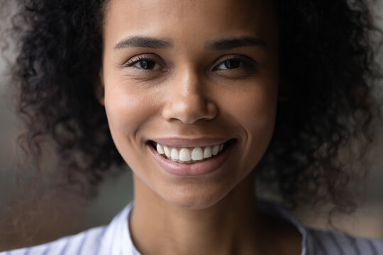Head shot close up of beautiful African American woman face, curly brunette attractive young female with healthy toothy smile and perfect smooth skin looking at camera, oral hygiene or skincare