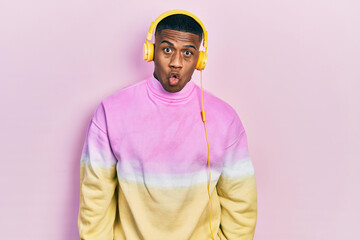 Young black man listening to music wearing headphones afraid and shocked with surprise expression, fear and excited face.