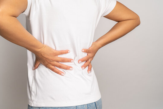 Female holding hands on back suffer from chronic backache. Cropped image of african woman with painful lower lumbar, spinal or kidney ache, periodic pain syndrome. Healthcare and massage treatment