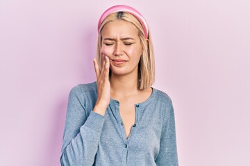 Beautiful blonde woman standing over pink background touching mouth with hand with painful expression because of toothache or dental illness on teeth. dentist