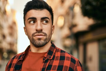 Young hispanic man with serious expression standing at the city.