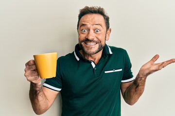 Middle age man drinking a cup of coffee celebrating achievement with happy smile and winner...