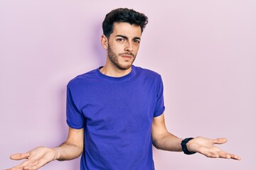 Young hispanic man wearing casual t shirt clueless and confused with open arms, no idea concept.