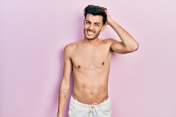 Fototapeta premium Young hispanic man wearing swimwear shirtless confuse and wonder about question. uncertain with doubt, thinking with hand on head. pensive concept.