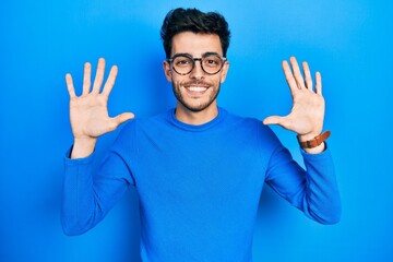 Young hispanic man wearing casual clothes and glasses showing and pointing up with fingers number ten while smiling confident and happy.